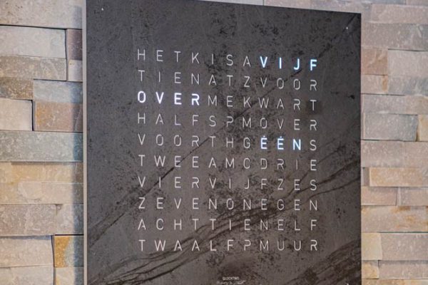 QLOCKTWO woordklok met letterraster aan een stenen wand